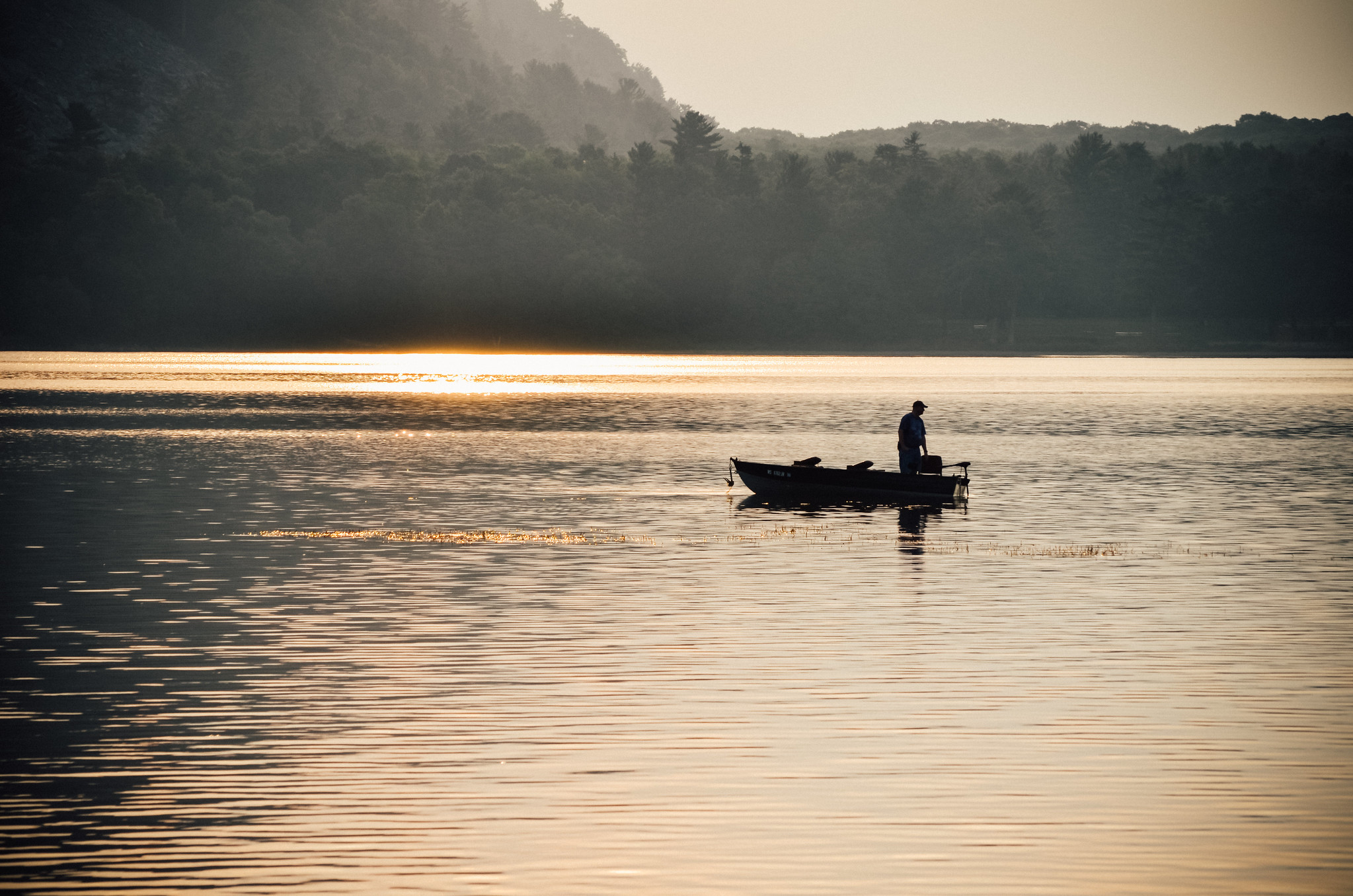 Person fishing from a boat in the middle of a Wisconsin lake early in the morning.