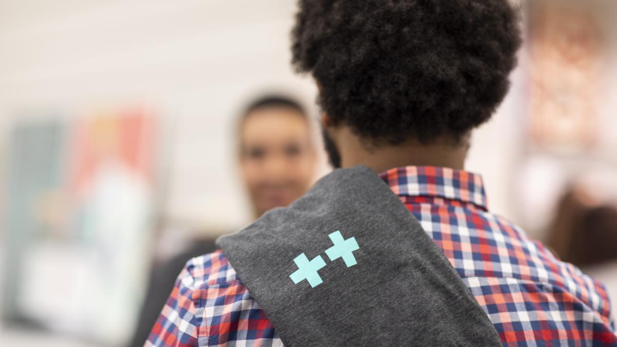 Photo of a man from behind with a ++ sweatshirt draped over his shoulder