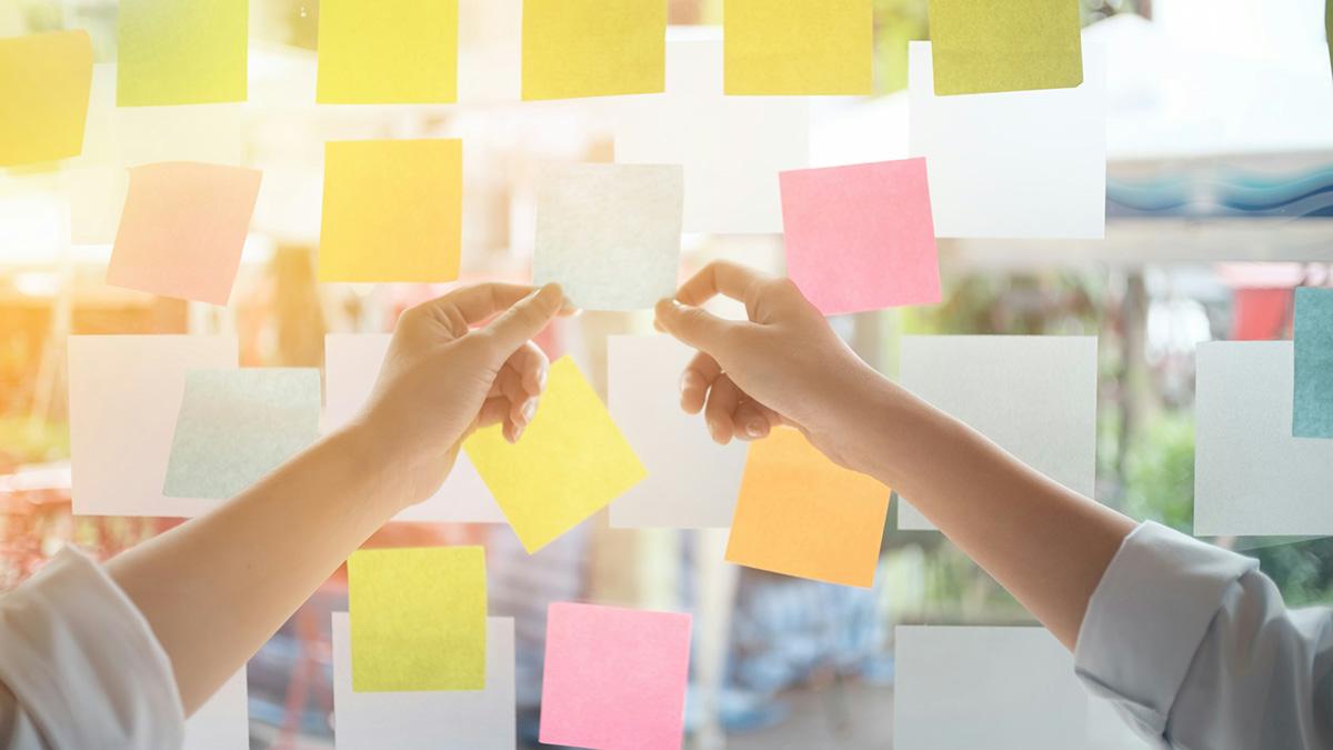 Close-up of hands arranging a variety of colorful sticky notes on a glass window, likely for brainstorming or project planning.