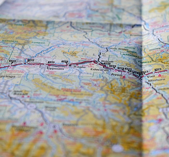 Asection of a road map showing various locations, routes, and landmarks. There are highways marked in black and red, with towns and cities such as Glenwood Springs, Gypsum, and Edwards labeled. Surrounding areas include natural features like national forests. The map is slightly folded, giving it a 3D texture.