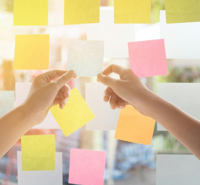 Close-up of hands arranging a variety of colorful sticky notes on a glass window, likely for brainstorming or project planning.