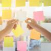 Close-up of hands arranging a variety of colorful sticky notes on a glass window, likely for brainstorming or project planning.